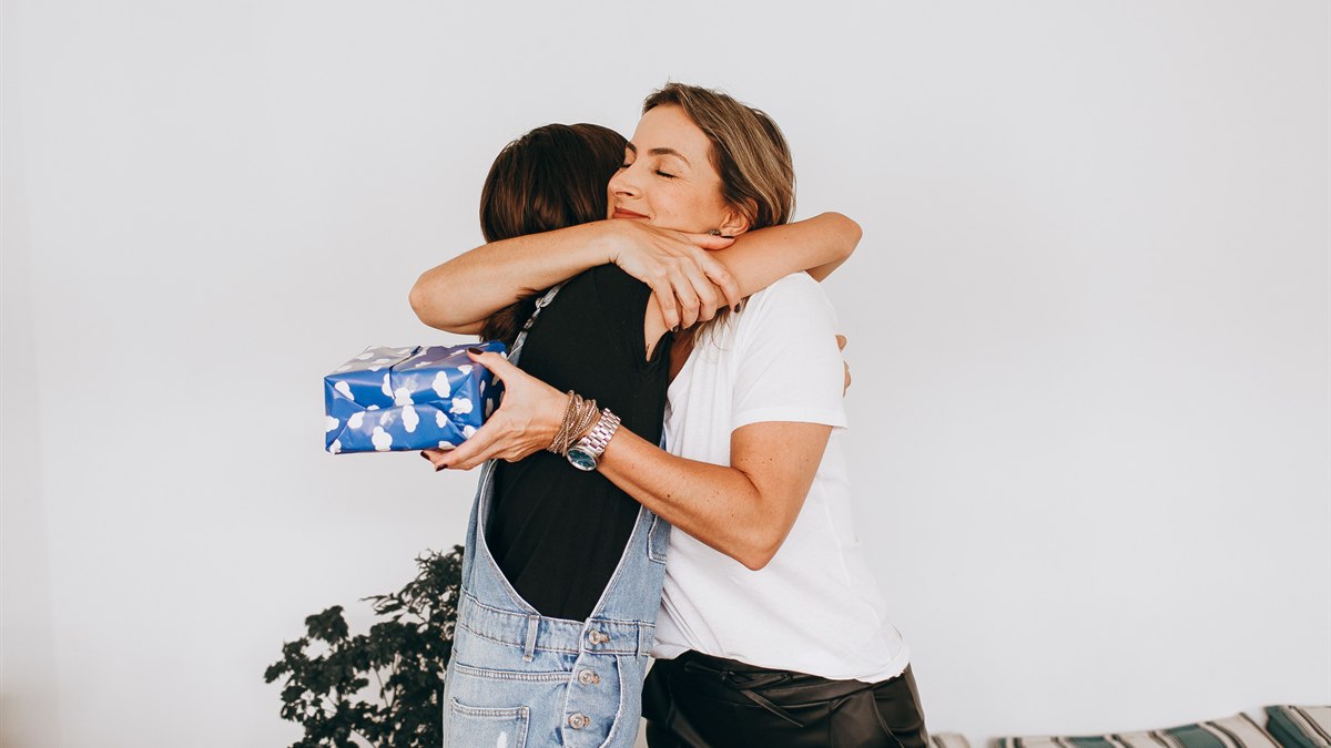Duas mulheres abraçam-se enquanto uma segura uma prenda embrulhada em papel azul